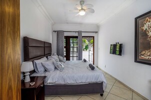 Un dormitorio con cama, mesita de noche, lámpara, cortinas y ventilador de techo.