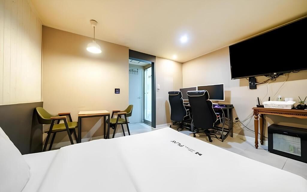 Habitación de hotel con cama, escritorio, sillas, televisor y ventana.
