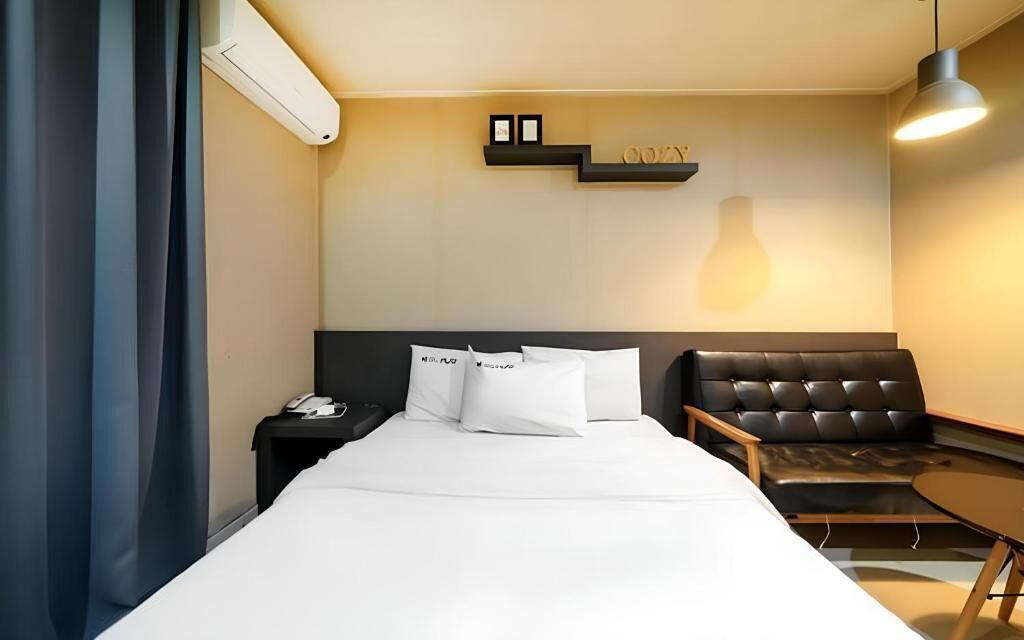 Habitación de hotel con cama, mesita de noche, teléfono, sofá y una pequeña mesa.