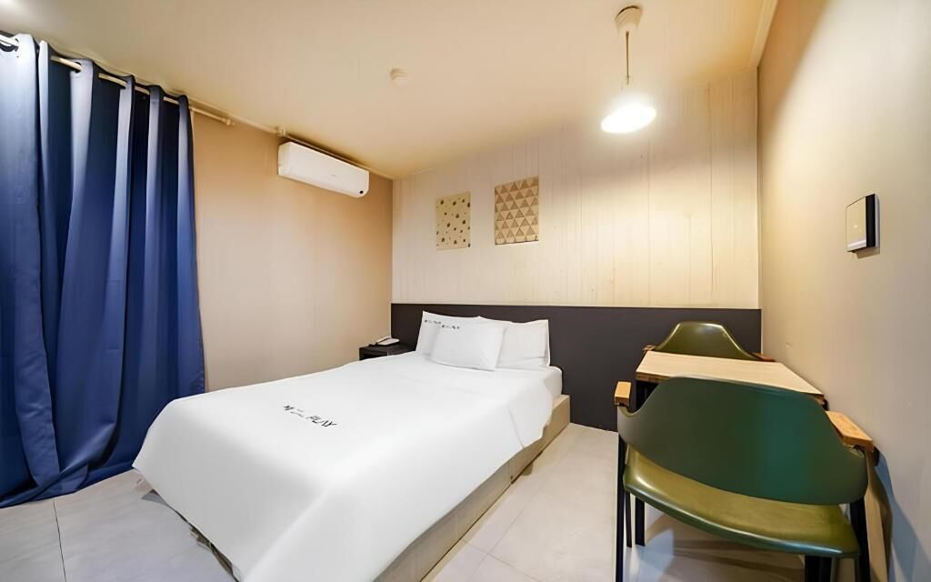 Quarto de hotel com cama, escrivaninha, cadeira e cortina.