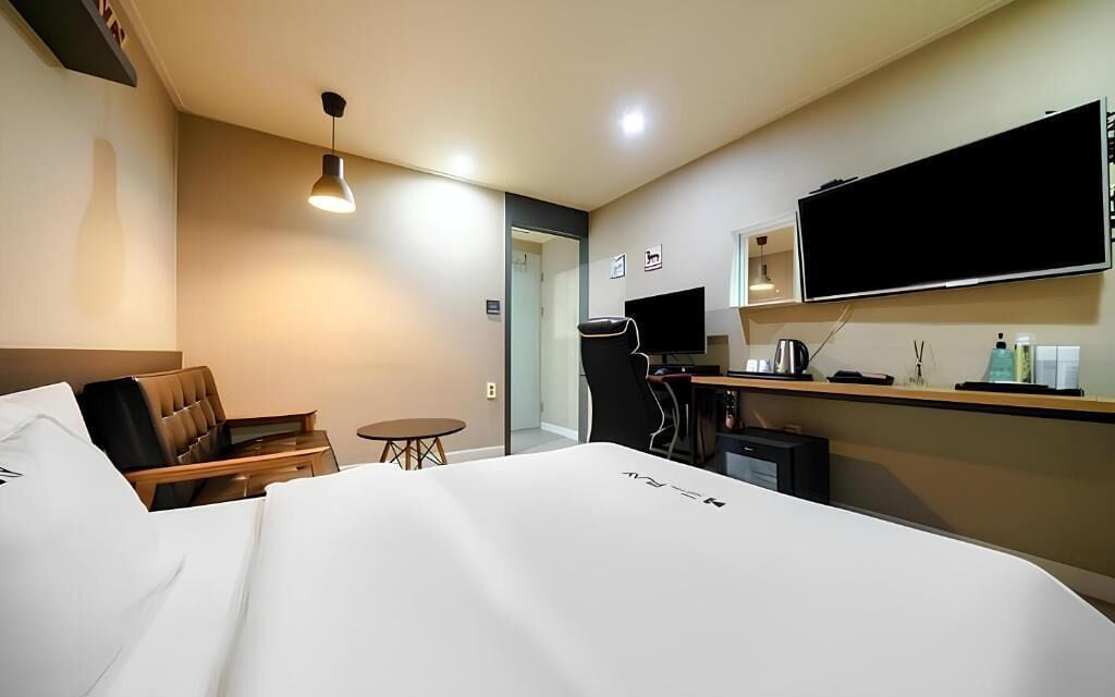 Ein Hotelzimmer mit einem Bett, einem Schreibtisch, einem Stuhl, einem Fernseher und einem kleinen Tisch.