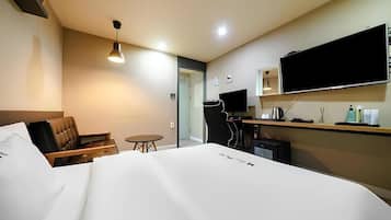 A hotel room with a bed, a desk, a chair, a television, and a small table.