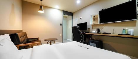 Habitación de hotel con cama, escritorio, silla, televisor y una mesita.