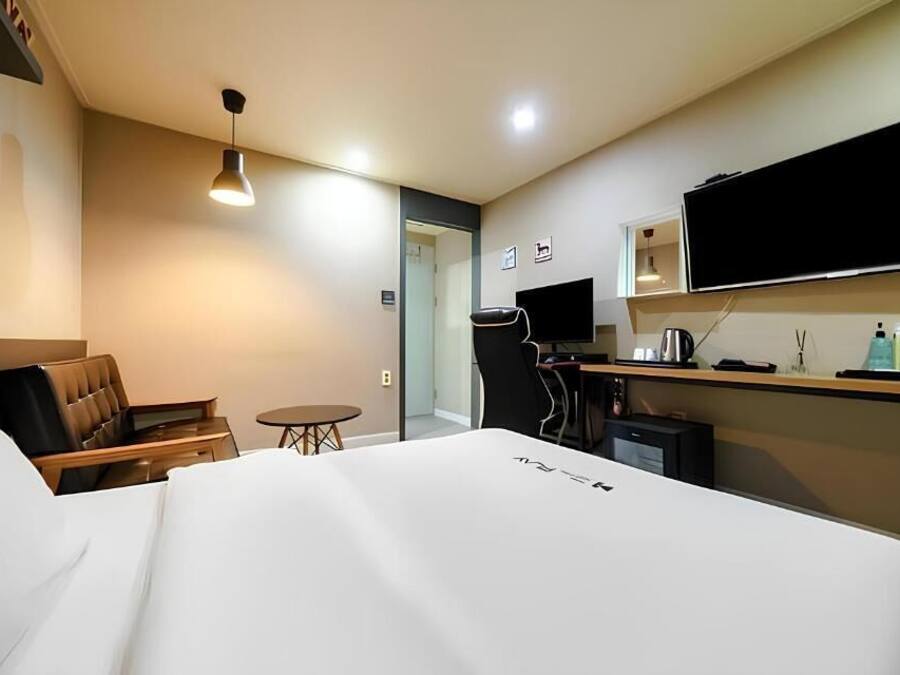 Habitación de hotel con cama, escritorio, silla, televisor y una mesita.