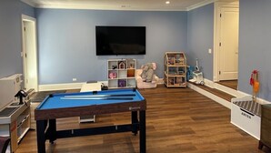 Ein Zimmer mit Billardtisch, einem an der Wand befestigten Fernseher und einem Bücherregal mit Spielzeug.