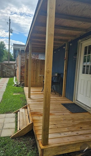 Una terraza de madera con un porche cubierto, un muro de ladrillo y una puerta de acceso al garaje.