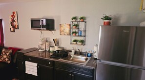 A kitchen with a stainless steel refrigerator, a microwave, and a coffee maker on the counter. There are potted plants on shelves and a painting on the wall. - Cozy 1-bedroom house in adorable Pensacola with AC (Pensacola)