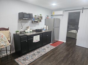 A compact kitchen with a microwave, refrigerator, and a small dining area with a chair and table. - Cozy 1-bedroom house in adorable Pensacola with AC (Pensacola)