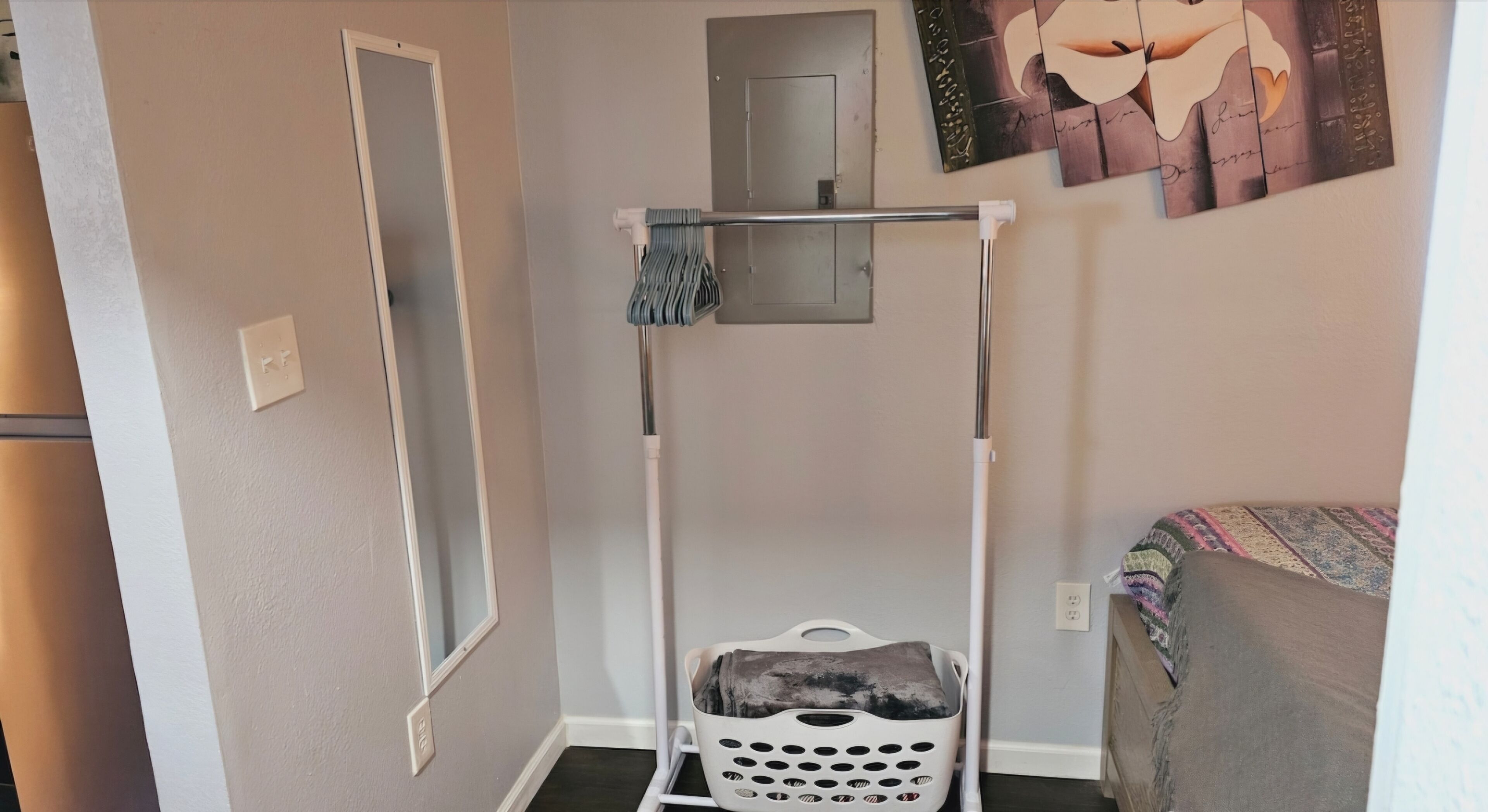 Une petite pièce comprenant un étendoir à linge, une porte, une œuvre d’art accrochée au mur et un lit recouvert d’une couverture à motifs.