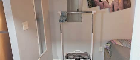 Une petite pièce comprenant un étendoir à linge, une porte, une œuvre d’art accrochée au mur et un lit recouvert d’une couverture à motifs.