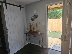 A room with a wooden door, a small table with a ship model, and a view of a wooden deck outside. - Cozy 1-bedroom house in adorable Pensacola with AC (Pensacola)