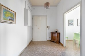 Um corredor com uma porta branca, um pequeno armário e uma cadeira verde.