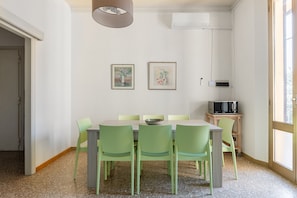 A dining area with a table and chairs, an air conditioning unit, and artwork on the wall. - Irnerio Apts - Olive Green by Wonderful Italy (Bologna)