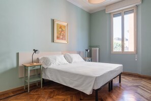 Ein Schlafzimmer mit einem Bett, einem Nachttisch, einer Lampe, einem Heizkörper und einem Fenster.