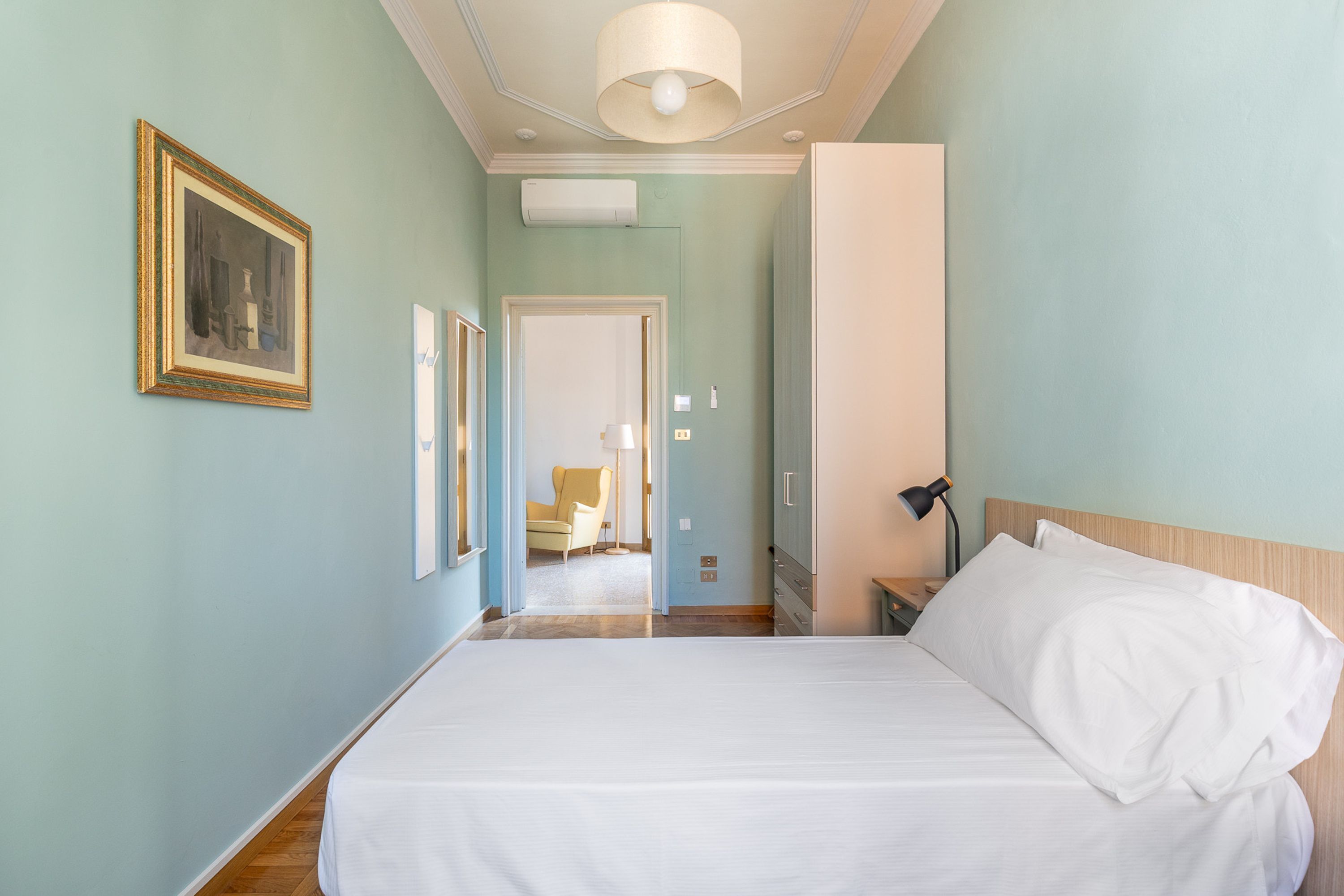 Une chambre d’hôtel avec un grand lit, une table de chevet, une lampe et une porte donnant sur une autre pièce.