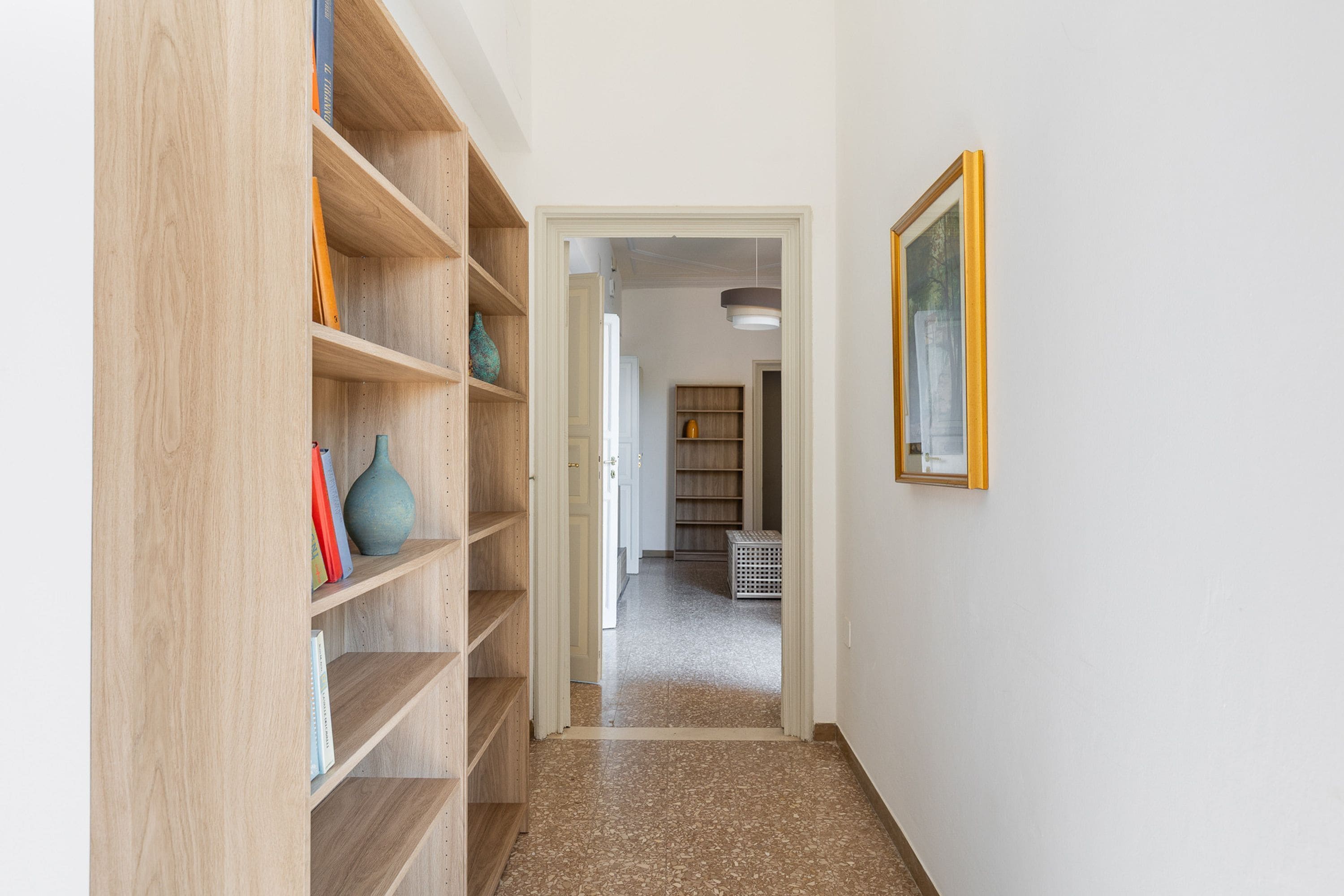Ein Flur mit einer Holzbücherwand, einer Tür zu einem anderen Raum und einem gerahmten Bild an der Wand.