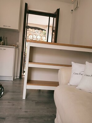 A bunk bed with a wooden headboard, a white sofa with pillows, and a kitchen area with wine bottles. - Casa Panorama — 50 square meters of garden with a hot tub and a view of the lake (Laino)