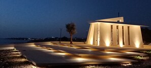 A modern building with a unique architectural design, featuring a series of vertical columns and a sloped roof. - Venus Beach Apartment. Diana 33 (Pafos)