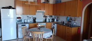 A kitchen with wooden cabinets, a refrigerator, a microwave, a coffee maker, and a washing machine. - Venus Beach Apartment. Diana 33 (Pafos)