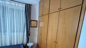 Een slaapkamer met een bed, een kledingkast, een klein krukje en een raam met gordijnen.