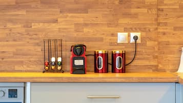 A kitchen with a wooden backsplash, a coffee maker, two red containers, and a clock.