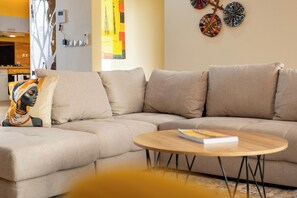 A modern living room with a sectional sofa, a round wooden coffee table, and decorative wall art. - Villa Banka - Banfeko Loft, Ground Floor (Dangane)