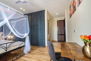 A bedroom with a bed, a bedside table, a chair, a wooden table, a vase with flowers, a ceiling fan, and a door. - Villa Banka - Banfeko Loft, Ground Floor (Dangane)