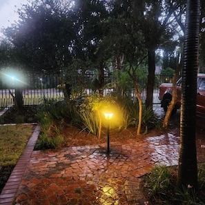 A paved pathway with a street lamp, surrounded by greenery and a fence.