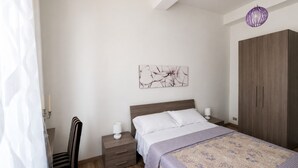 A bedroom with a bed, a nightstand, a chair, a wardrobe, and a wall art piece. - Elegant apartment just a stone's throw from Piazza del Campo (Siena)