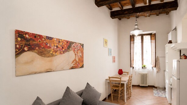 A cozy living area with a sofa, a dining table, and a kitchen with a refrigerator. - Elegant apartment just a stone's throw from Piazza del Campo (Siena)