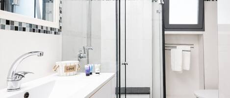 A modern bathroom with a glass-enclosed shower, a white sink with a chrome faucet, and a mirror above the sink.