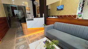 A reception area with a sofa, a reception desk, a clock, and a TV on the wall.