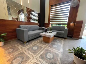 A modern lobby with a grey sectional sofa, a coffee table, and a patterned rug. - Hotel Royal Aana Inn (Jaipur)