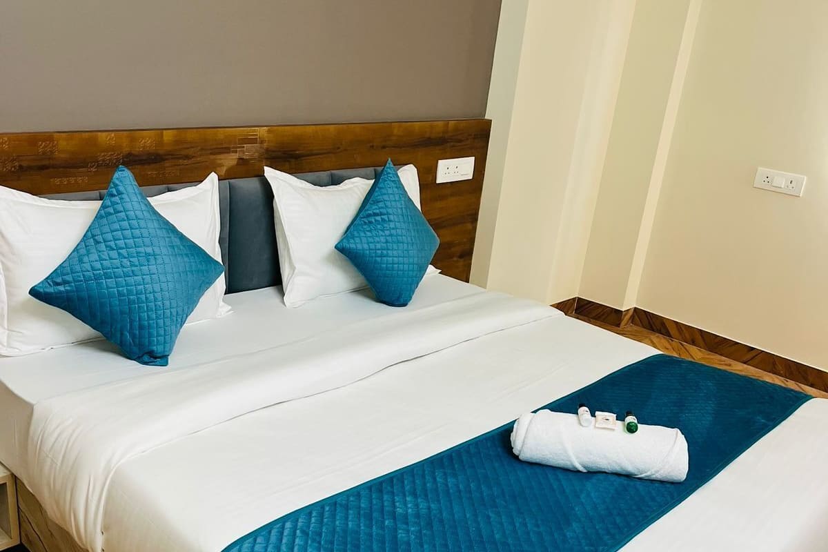 A neatly made bed with a wooden headboard, white bedding, and two blue pillows.