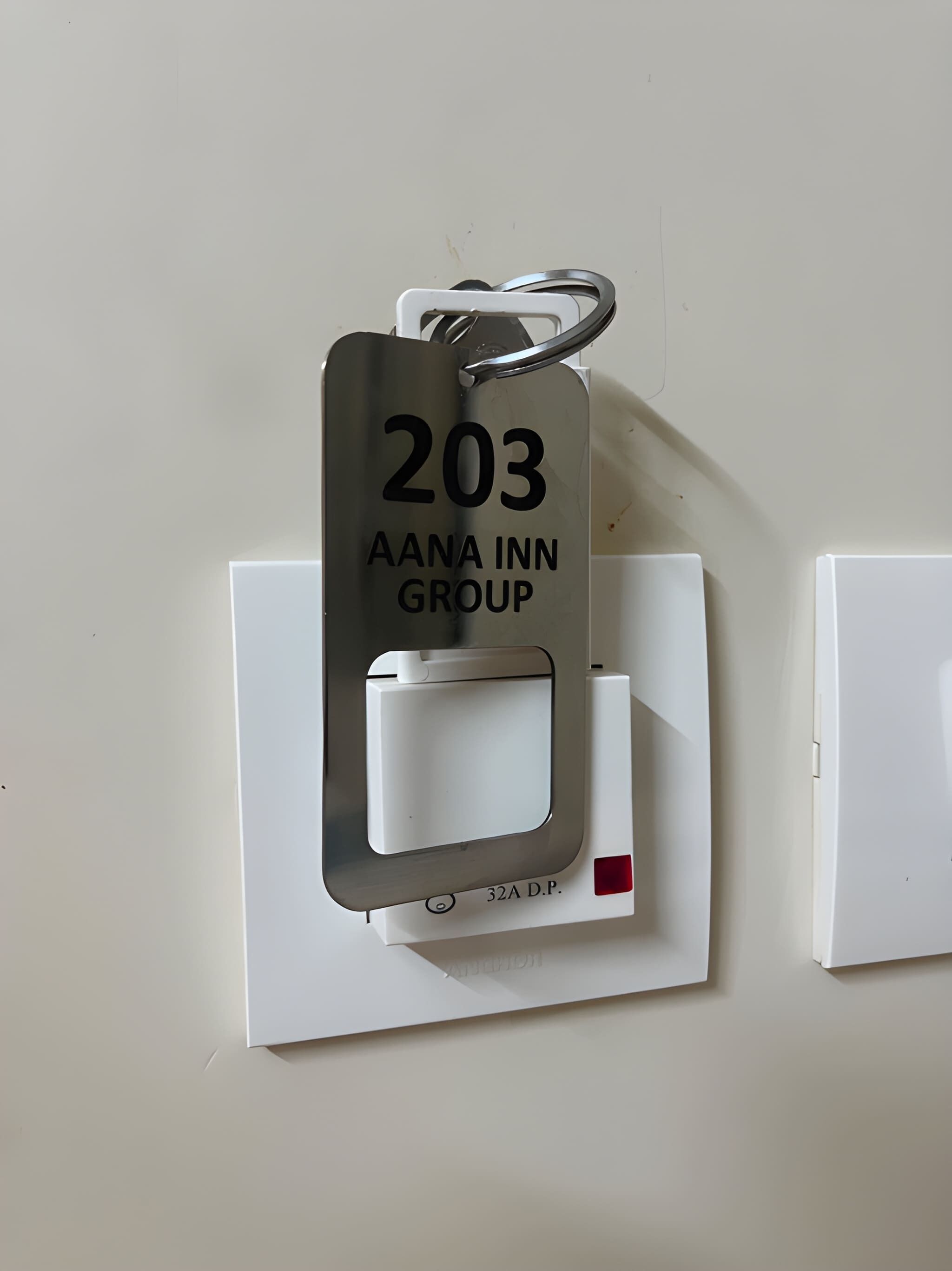 Una llave de acceso con '203 AANA INN GROUP' y '32A D.P.' en un interruptor fijado a la pared.