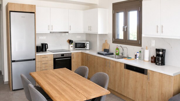 A modern kitchen with white cabinets, a wooden dining table, and grey chairs. - Zidros Apartments Maisonette Apartment 4 (Sfakaki)