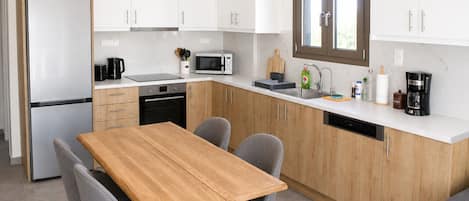 A modern kitchen with white cabinets, a wooden dining table, and grey chairs.