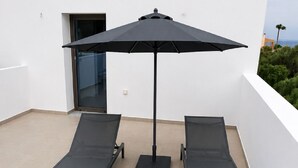 A rooftop terrace with two sun loungers, a small table, and a large umbrella. - Zidros Apartments Maisonette Apartment 4 (Sfakaki)