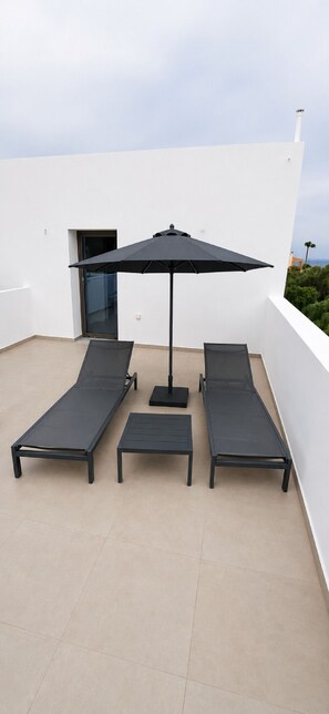 A rooftop terrace with two sun loungers, a small table, and a large umbrella. - Zidros Apartments Maisonette Apartment 4 (Sfakaki)