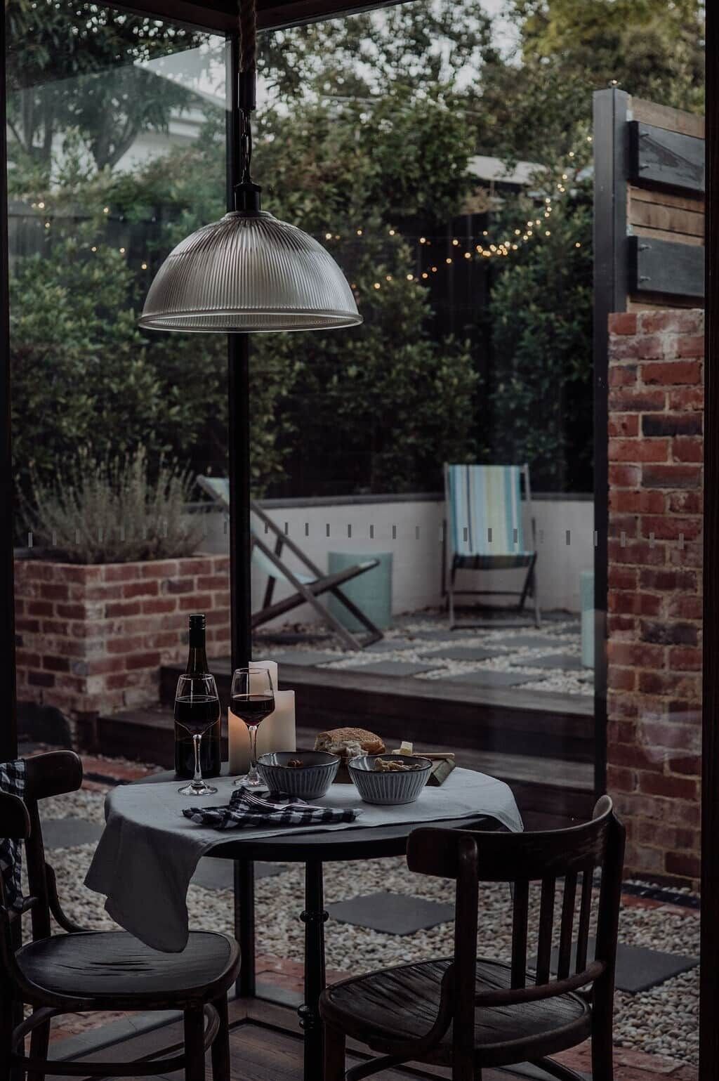 A patio with a table set for dining, a bottle of wine, and candles.