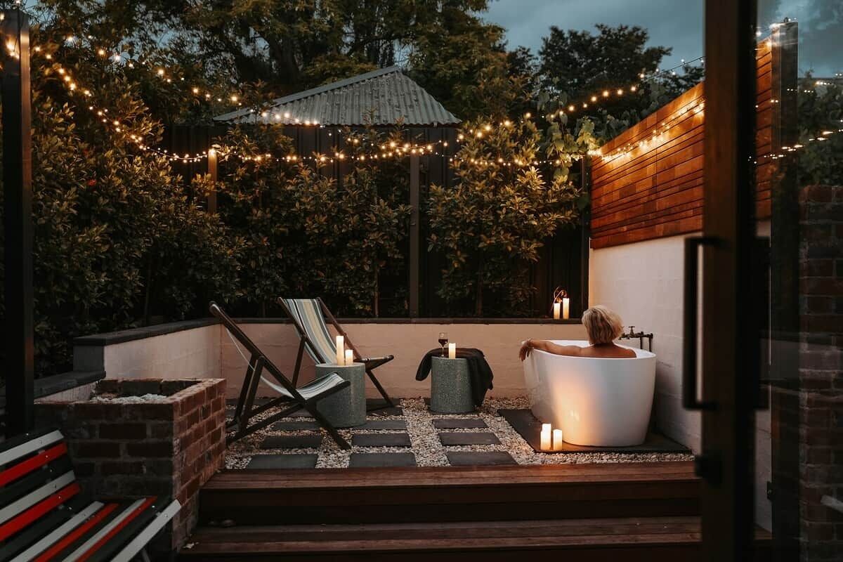 An outdoor patio with a seating area, a bathtub, and string lights.