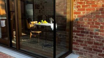 A glass door leading to a patio area with a table and chairs, a brick wall, and a gravel ground.