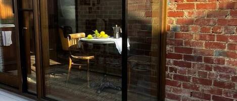 Une porte vitrée donne sur un patio aménagé avec une table et des chaises, un mur en briques et un sol en gravier.