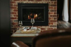 A cozy room with a fireplace, two glasses of wine, and a small table with a book and a candle. - Braithwaite: Chic Pied-a Terre with Fireplace + Outdoor Bath (Sandy Bay)