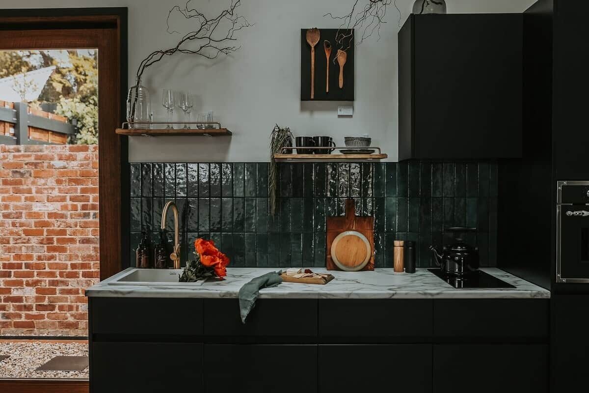 A kitchen with a brick wall, a black countertop, and a wooden cutting board.