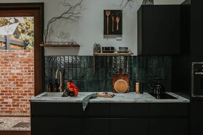 A kitchen with a brick wall, a black countertop, and a wooden cutting board. - Braithwaite: Chic Pied-a Terre with Fireplace + Outdoor Bath (Sandy Bay)