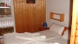 A bedroom with a wooden headboard, a bed with white bedding, a nightstand with a lamp, and a window with curtains. - Praktischer Doppelbungalow mit Terrasse im Ferienpark Mirow (Mirow)