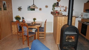 A cozy living room with a sofa, wooden dining table, chairs, and a wood-burning stove. - Praktischer Doppelbungalow mit Terrasse im Ferienpark Mirow (Mirow)