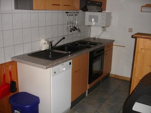 A compact kitchen with a dishwasher, stove, microwave, and a sink. - Praktischer Doppelbungalow mit Terrasse im Ferienpark Mirow (Mirow)