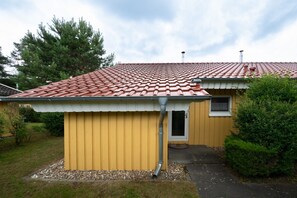 A single-story house with a red-tiled roof, a yellow exterior, and a small front porch. - Praktischer Doppelbungalow mit Terrasse im Ferienpark Mirow (Mirow)